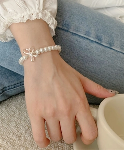 Elegant white round pearl bracelet with a silver bow charm worn on the wrist