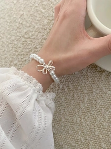 Close-up of elegant pearl bead bracelet with silver bow charm worn on wrist