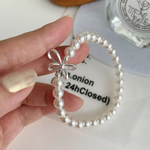 Detail view of round white pearl bracelet with delicate silver bow charm on a hand