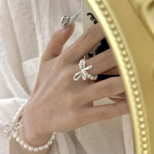 Detailed close-up of a white pearl ring and bracelet with silver bow accents on hand