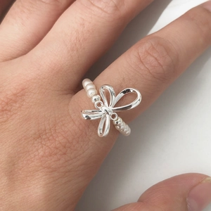 Detail of silver bow ring with white pearls on finger, sweet and elegant jewelry style