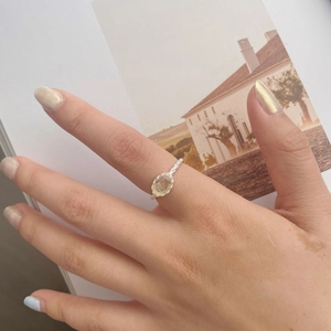 Detailed view of an oval yellow crystal ring on a finger with a woven silver band texture