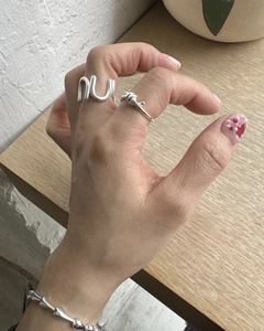 Detail shot of a silver knot ring and wavy letter ring worn on a hand over a wooden desk