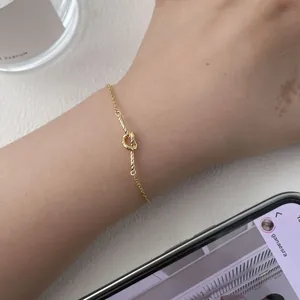 Detailed close-up of a gold woven knot bracelet on a wrist with minimalist design