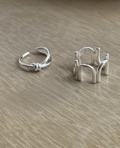 Detail of silver knot ring and architectural wave band on light wood background