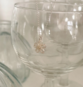 Close-up of a S925 silver necklace featuring a delicate hollow floral pendant on a glass