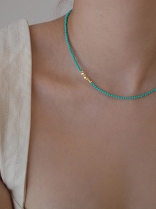 Close-up of turquoise beaded necklace with golden square spacer beads on neck