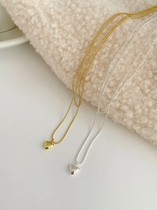 Detail shot of gold and silver heart necklaces with delicate bead chains on fabric