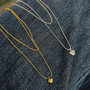 Close-up of gold and silver double-layered heart necklaces on blue denim fabric background