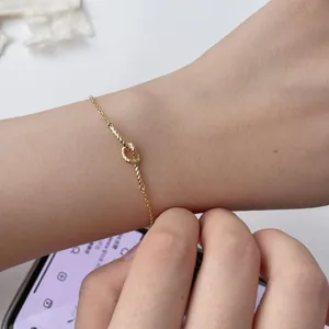 Close-up of a delicate golden braided heart knot bracelet on a woman's wrist