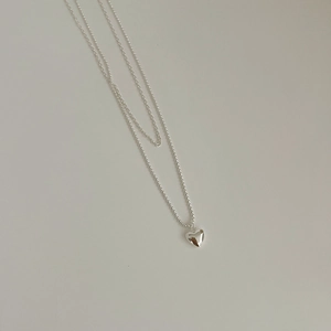 Detail of a silver double-layered necklace featuring a polished heart pendant and O-chains