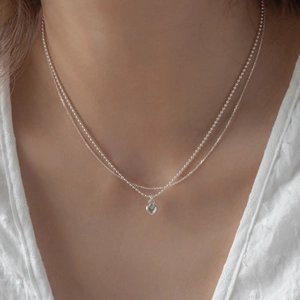Macro detail of double-layered silver heart necklace showing the bead and link chains