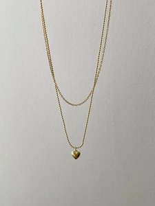 Detail of double-layer gold heart necklace featuring bead and cable chain textures