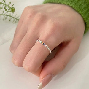 Rainbow gemstone ring on hand with green knit sleeve and nature background closeup