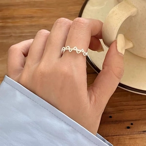 Dettaglio di un anello intrecciato minimalista argento al dito su sfondo caffè caldo