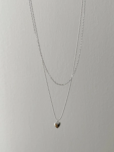 Close-up of double layer silver necklace featuring a beaded chain and heart pendant