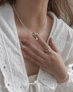 Detail view of silver heart pendant layered necklace and pearl ring on white lace shirt