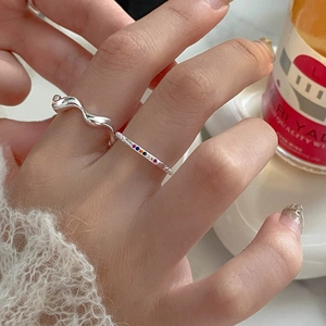 Close-up of stacked S925 silver wave ring and mini rainbow gemstone ring on finger