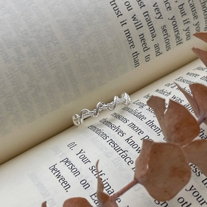 Dettaglio di un anello intrecciato in argento posto su un libro aperto con foglie secche