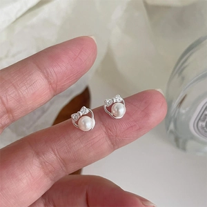 999 Sterling silver bow pearl earrings with cubic zirconia shown on fingertips