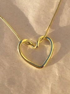 Detail eines minimalistischen Herzanhängers in Gold mit polierter Oberfläche an einer Kette