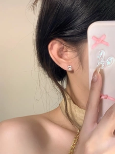 Detail view of silver bow stud earrings with white pearl accent on female model