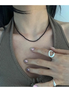 Detail of minimalist black beaded necklace and silver irregular lava rings on model