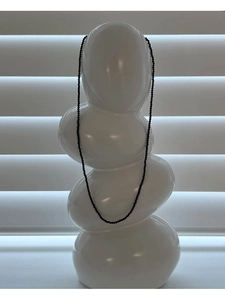 Macro detail of minimalist black spinel beaded necklace draped on white ceramic decor