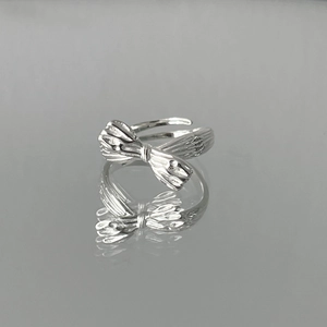 Silver bow ring with textured finish and adjustable open design on a reflective base