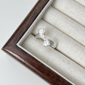 Detail view of a silver bow-knot ring with ribbon texture inside a velvet jewelry box