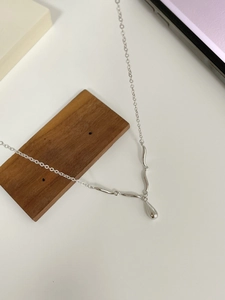 Macro view of minimalist S925 sterling silver necklace featuring wave charms and water drop