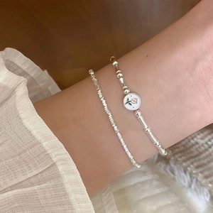 Detail of layered S925 silver bracelet featuring pink tulip charm and textured beads