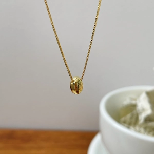 Detailed view of a polished gold oval bean pendant on a delicate box chain necklace