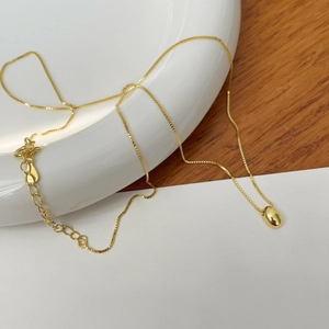 Detailed shot of a gold oval bean pendant necklace with box chain and lobster clasp