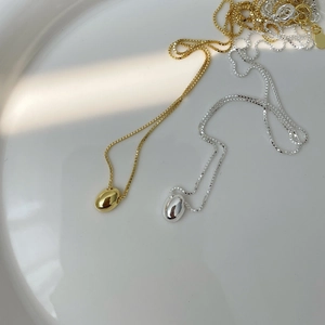 Macro detail of minimalist gold and silver oval bean pendants on delicate box chains