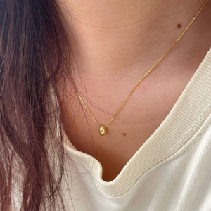 Minimalist gold bean pendant necklace worn by a model, showing dainty polished metal detail