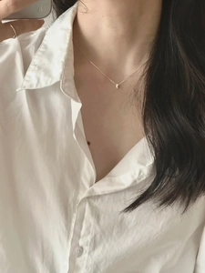 Close-up of a 925 silver bean pendant necklace and thin ring worn with a white shirt