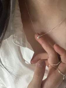 Close-up of minimalist S925 sterling silver bean necklace and rings worn by a model