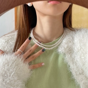 Close-up of double-layer white pearl necklace and stud earrings on model wearing white cardigan