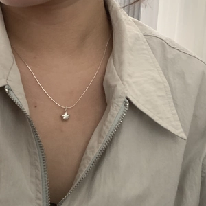 Close-up of a minimalist S925 silver star pendant necklace worn over a light jacket