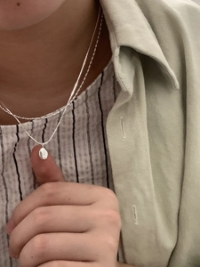 Detailed close-up of double-layer silver necklace with polished teardrop pendant on model
