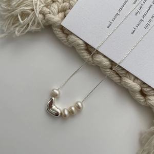 Detail view of irregular heart charm and freshwater pearls on an elegant silver chain