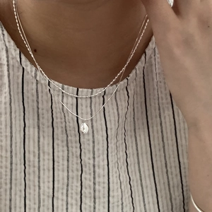 Detail of layered S925 silver necklace with oval pendant on white striped shirt
