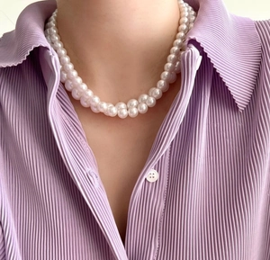 Detail of double-layer white pearl necklace worn with a purple textured shirt