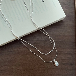 Detail of S925 silver double layer necklace with oval pendant on a dark wooden background