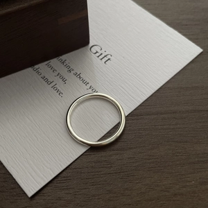 Gros plan d'une bague en argent poli minimaliste posée sur une carte cadeau blanche