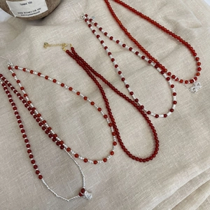 Macro view of red agate beaded necklaces with silver bow charms on linen background