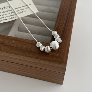 Detailed close-up of matte silver beads on a snake chain over a wood jewelry box