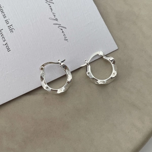 Dettaglio ravvicinato di orecchini a cerchio in argento S925 con trama metallica liquida