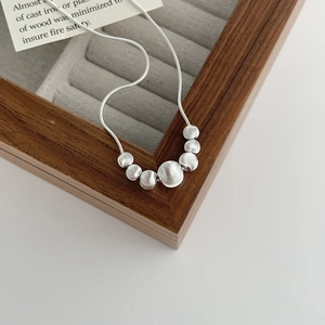 Detail of S925 silver beaded necklace with brushed metallic texture on a wooden box